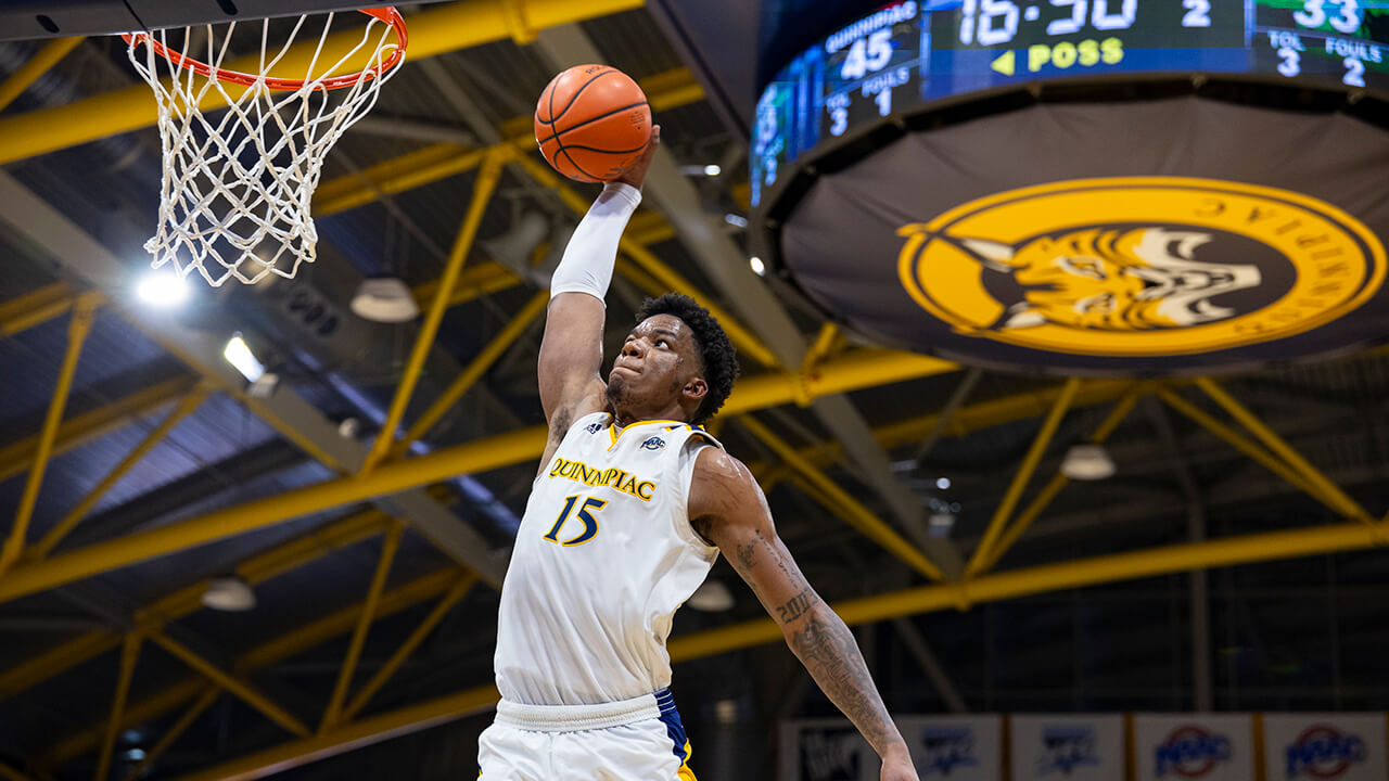 A Quinnipiac basketball player makes a shot with the scoreboard in the background